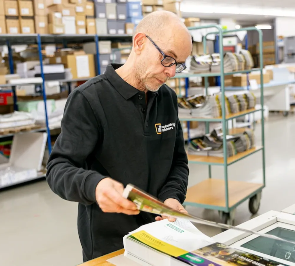 Medewerker van MarketingMakkers controleert drukwerk in werkruimte