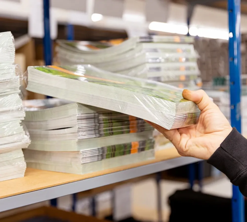 Hand pakt stapel drukwerk zoals brochures van plank