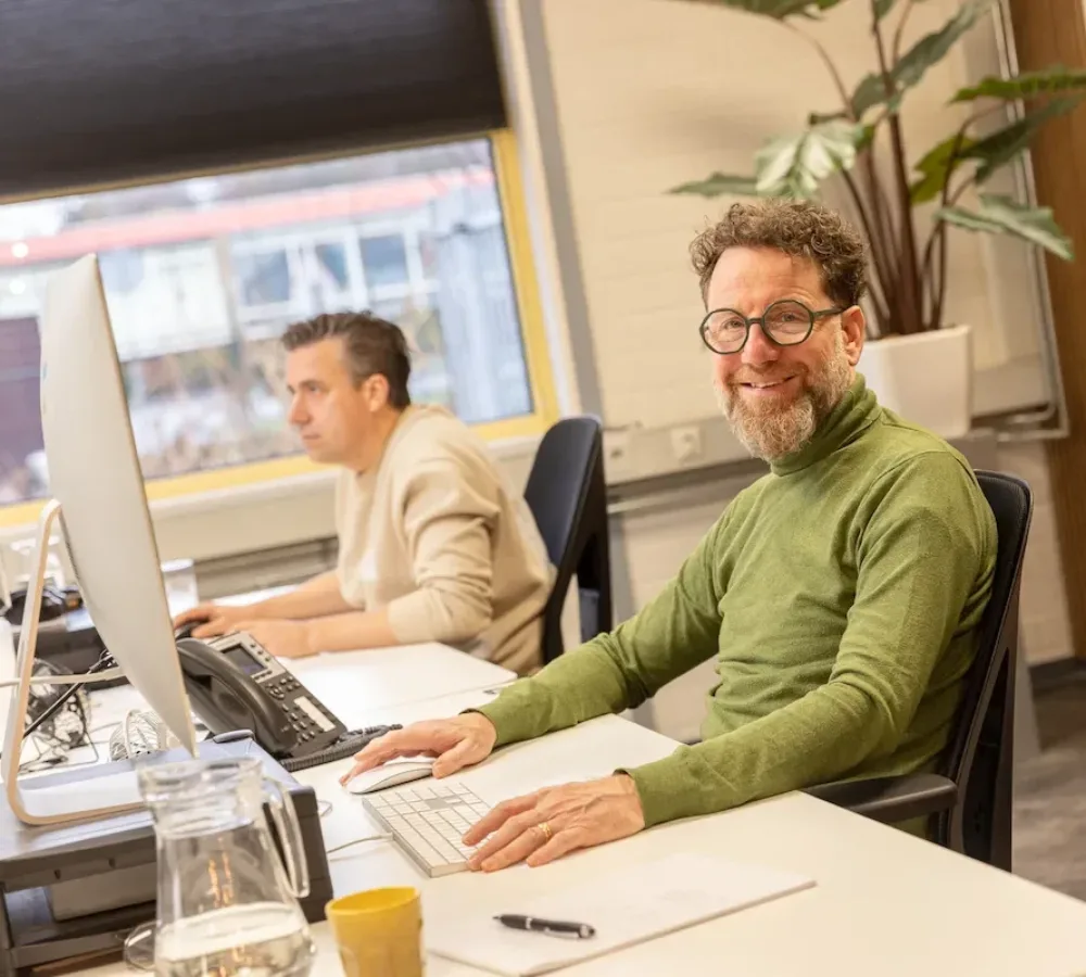 Twee medewerkers van MarketingMakkers werken aan drukwerk achter computer