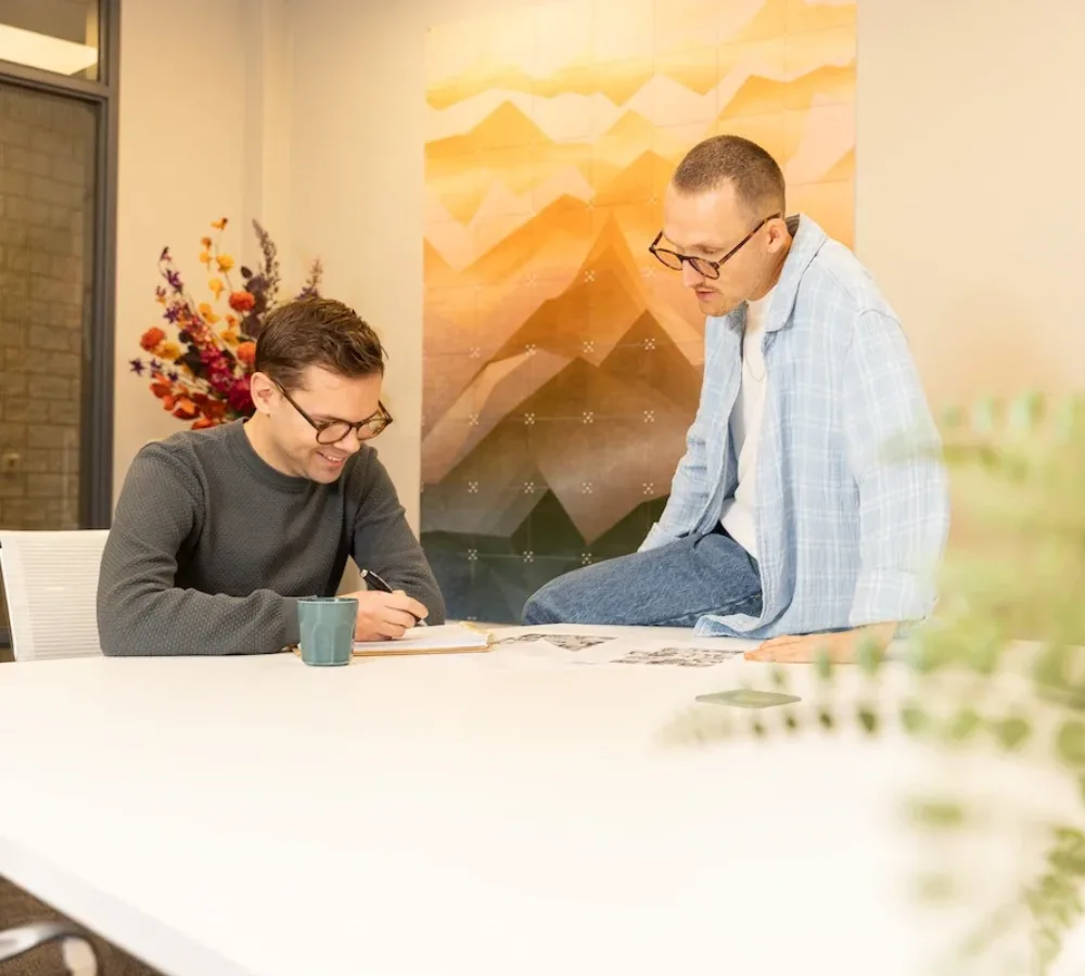 Twee medewerkers van MarketingMakkers bekijken samen werk aan tafel