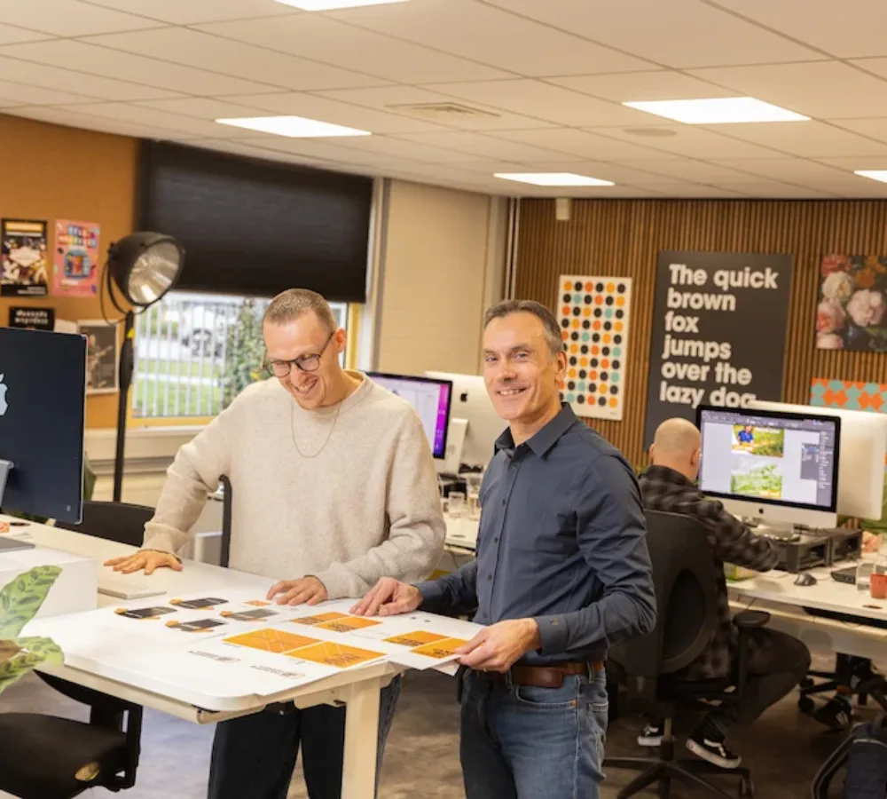 Twee vormgevers van MarketingMakkers bekijken drukwerk aan tafel